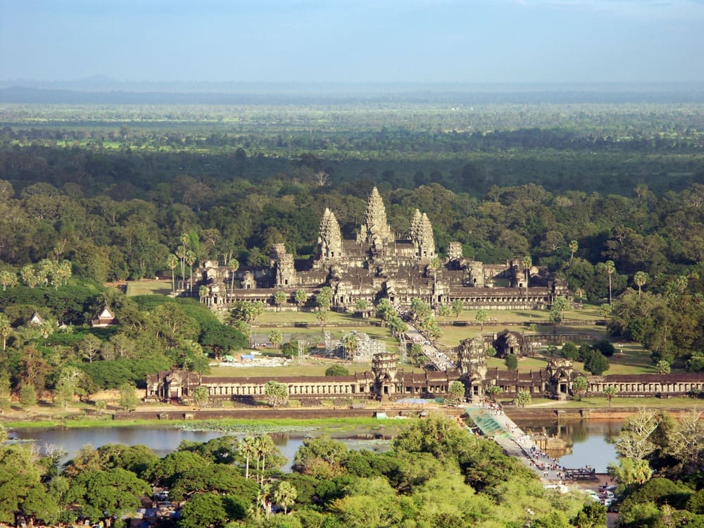 Angkor Wat's towers rising above forest beyond its moat and long entrance causeway, seen from the air